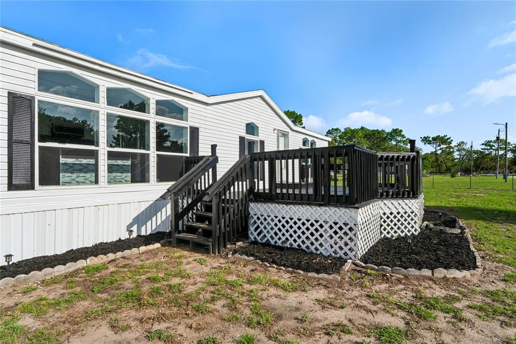 A white manufactured home features a black wooden deck with stairs and lattice skirting — 4357 ORLANDO AVENUE, BROOKSVILLE, FL