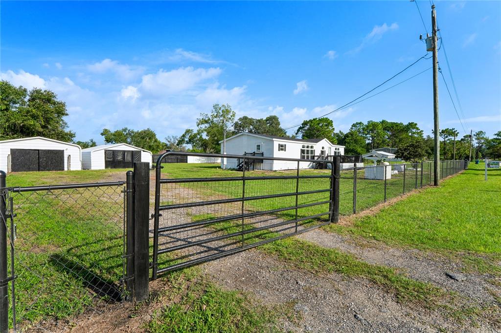 A white manufactured home sits behind a metal gate on a fenced, grassy lot — 4357 ORLANDO AVENUE, BROOKSVILLE, FL