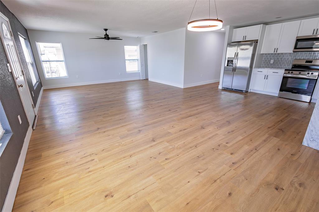A spacious room with light wood flooring, a ceiling fan, and an adjacent white kitchen — 4501 20TH AVENUE S, ST PETERSBURG, FL