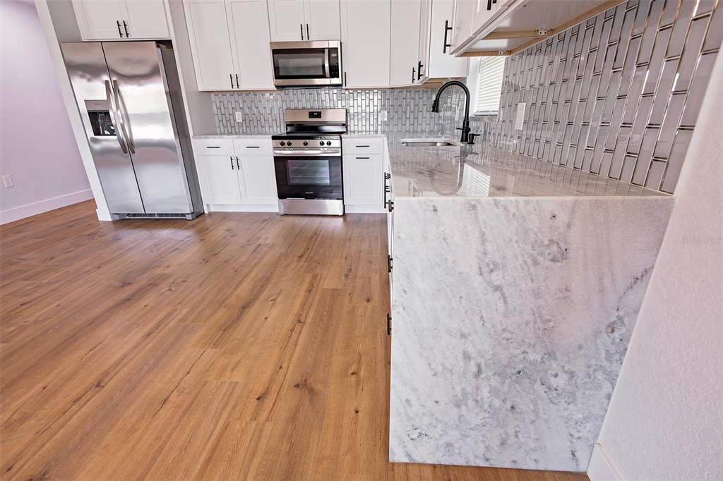 A kitchen features white cabinets, stainless steel appliances, a marble waterfall island, and wood flooring — 4501 20TH AVENUE S, ST PETERSBURG, FL
