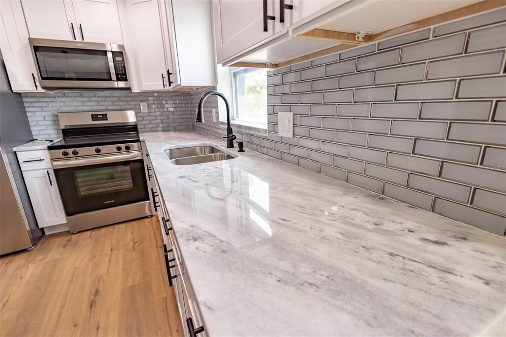 A modern kitchen features white cabinets, marble-look countertops, a stainless steel stove, and gray backsplash — 4501 20TH AVENUE S, ST PETERSBURG, FL