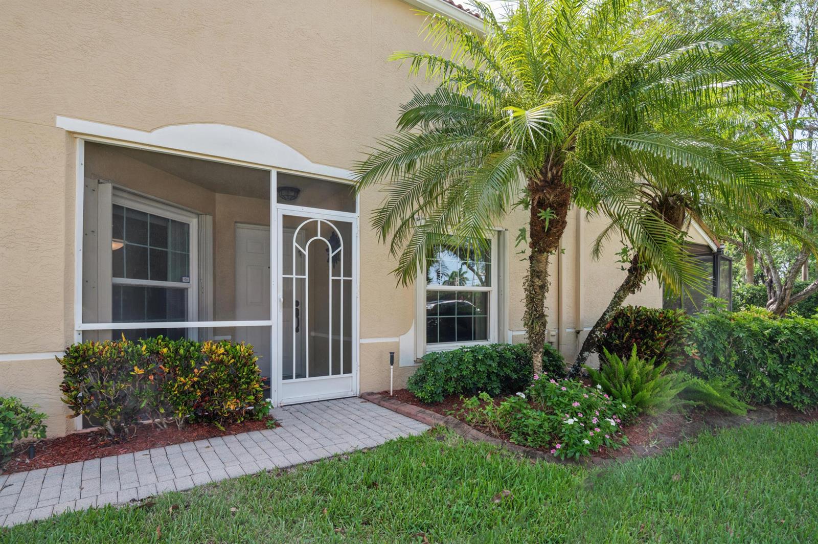 The exterior of a beige house features a screened entryway, a palm tree, and landscaping — 5053 TOSCANA Trail, Boynton Beach FL 33437, BOYNTON BEACH, FL