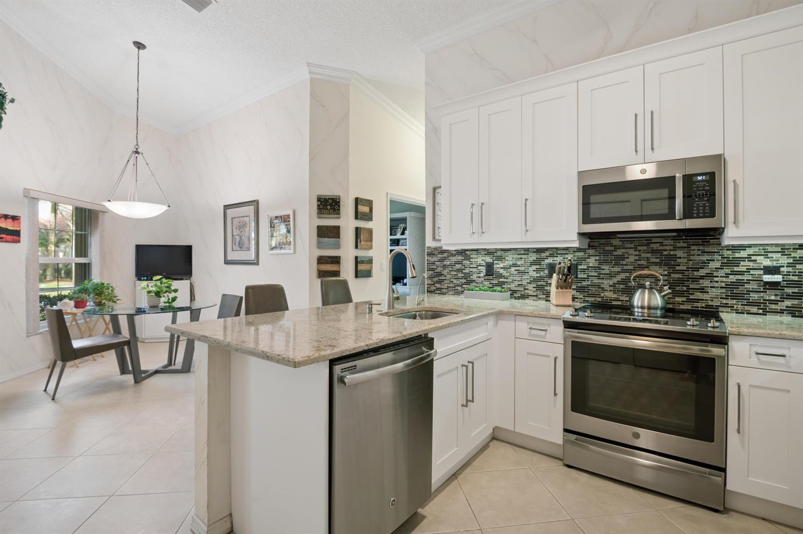 A kitchen with white cabinets, stainless steel appliances, and granite countertops overlooks a dining area — 5053 TOSCANA Trail, Boynton Beach FL 33437, BOYNTON BEACH, FL