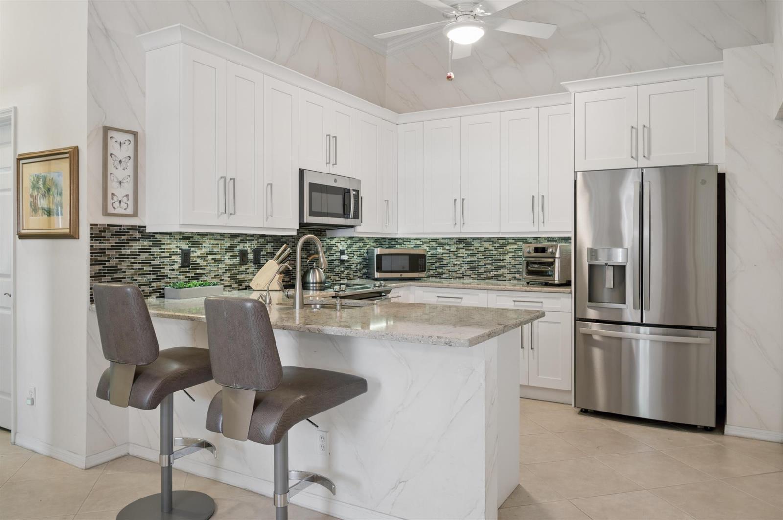 A kitchen features white cabinets, granite countertops, a mosaic backsplash, and two bar stools — 5053 TOSCANA Trail, Boynton Beach FL 33437, BOYNTON BEACH, FL