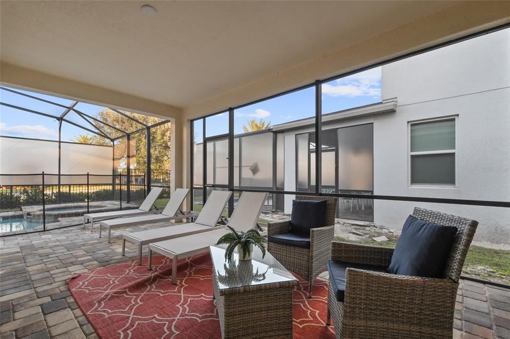 A covered patio features a brick floor, lounge chairs, wicker seating, and a screened enclosure — 8931 AMELIA DOWNS TRAIL, KISSIMMEE, FL