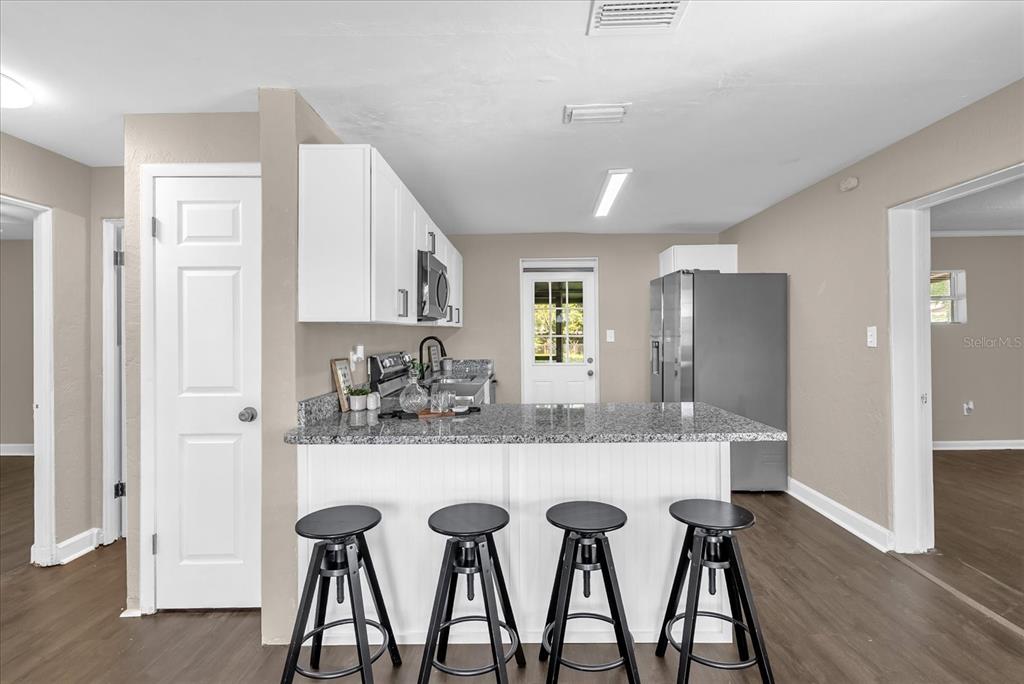 A kitchen features white cabinets, granite countertops, a breakfast bar with four stools, and stainless appliances — 461 BRENTWOOD DRIVE, DAYTONA BEACH, FL