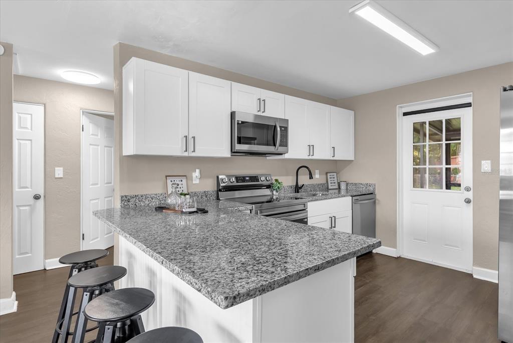 A kitchen features white cabinets, granite countertops, stainless steel appliances, and a breakfast bar with stools — 461 BRENTWOOD DRIVE, DAYTONA BEACH, FL