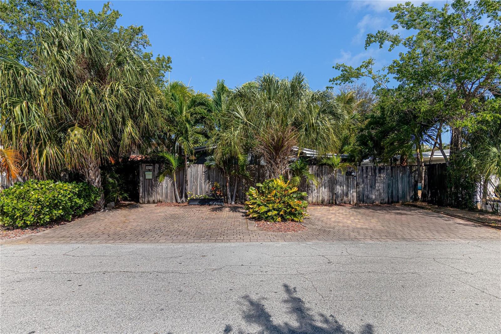 A paved driveway leads to a wooden fence surrounded by palm trees and lush landscaping — 1009 NE 23rd Drive, Wilton Manors FL 33305, WILTON MANORS, FL