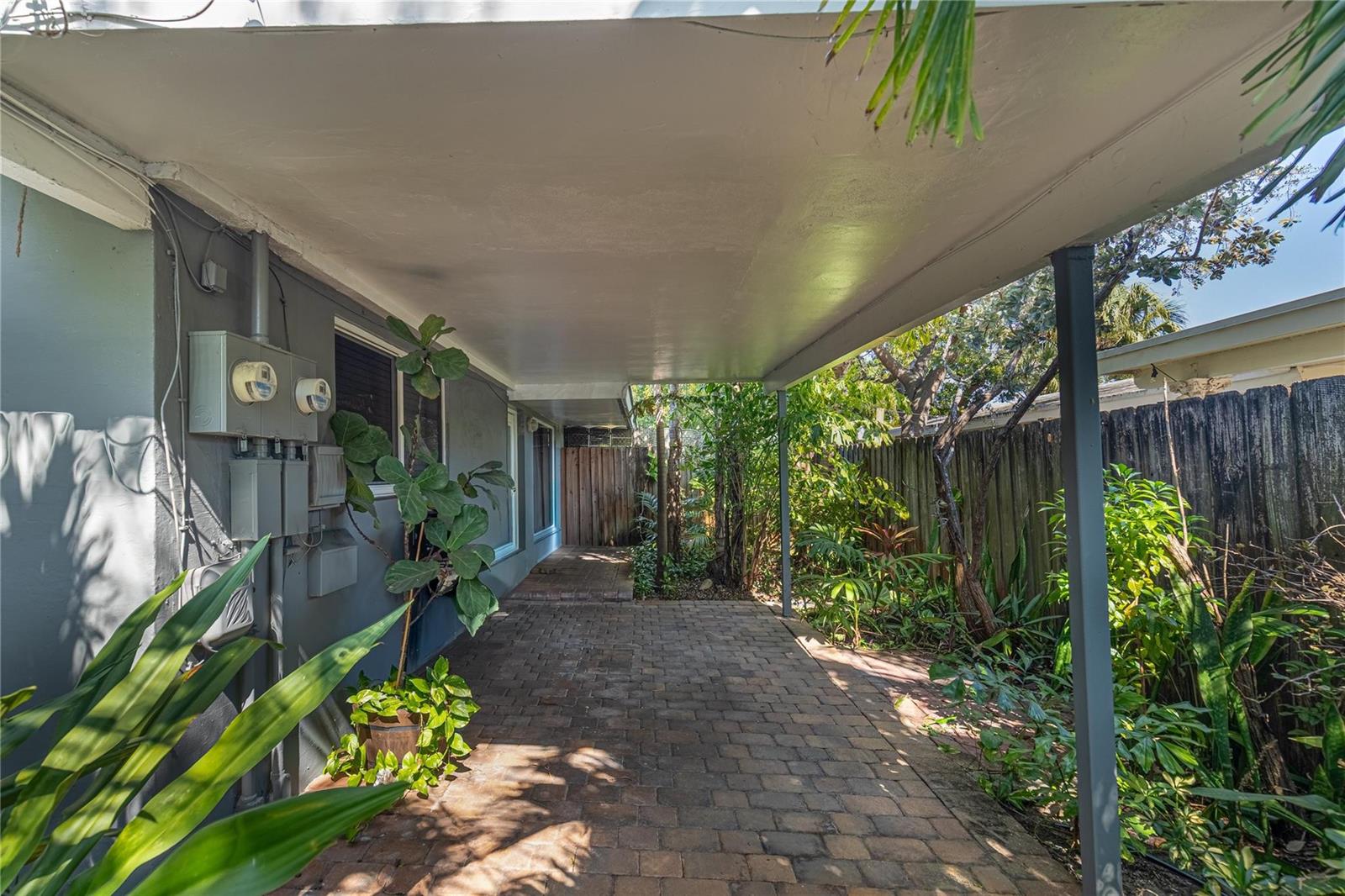 A covered brick patio area sits beside a gray house with lush tropical landscaping — 1009 NE 23rd Drive, Wilton Manors FL 33305, WILTON MANORS, FL