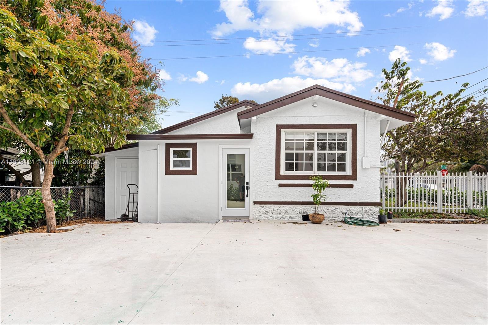 A single-story white house with brown trim features a concrete driveway and a white fence — 3902 NW 3rd Ave, Miami FL 33127, MIAMI, FL