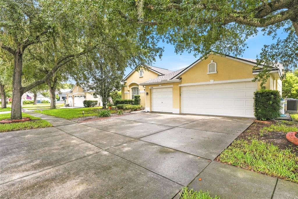 A yellow single-story house with a three-car garage and a concrete driveway — 16748 MIDSUMMER LANE, SPRING HILL, FL
