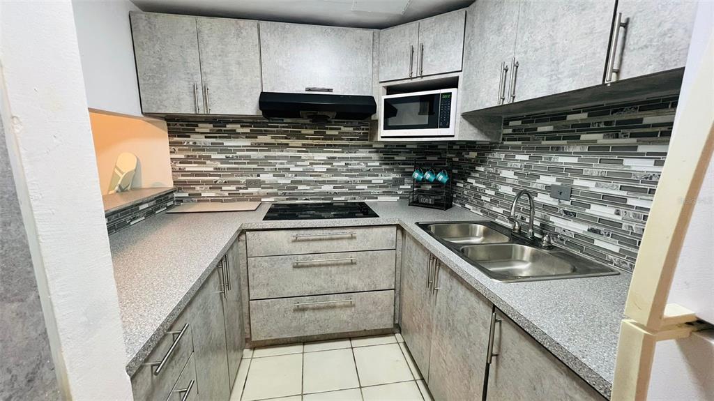 A kitchen features gray textured cabinets, a mosaic tile backsplash, and a double-basin stainless sink — 1015 HARBOURSIDE DR. UNIT 1015, HUMACAO, PR