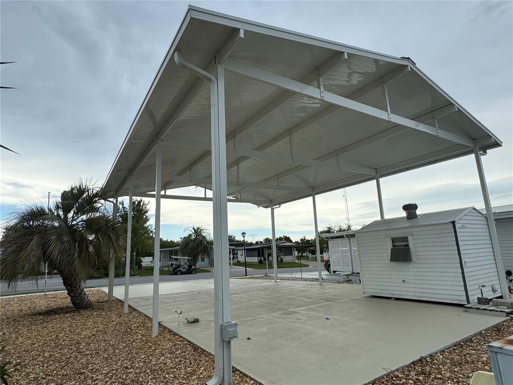 A large metal carport with a concrete slab sits next to a small white shed — 4842 BOBBY AVENUE Lot 198, ZEPHYRHILLS, FL