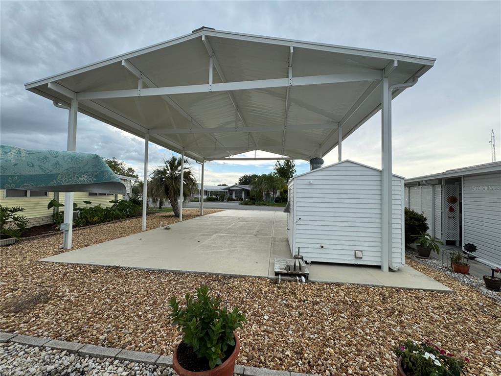 A large metal carport with a concrete pad and a small white storage shed — 4842 BOBBY AVENUE Lot 198, ZEPHYRHILLS, FL