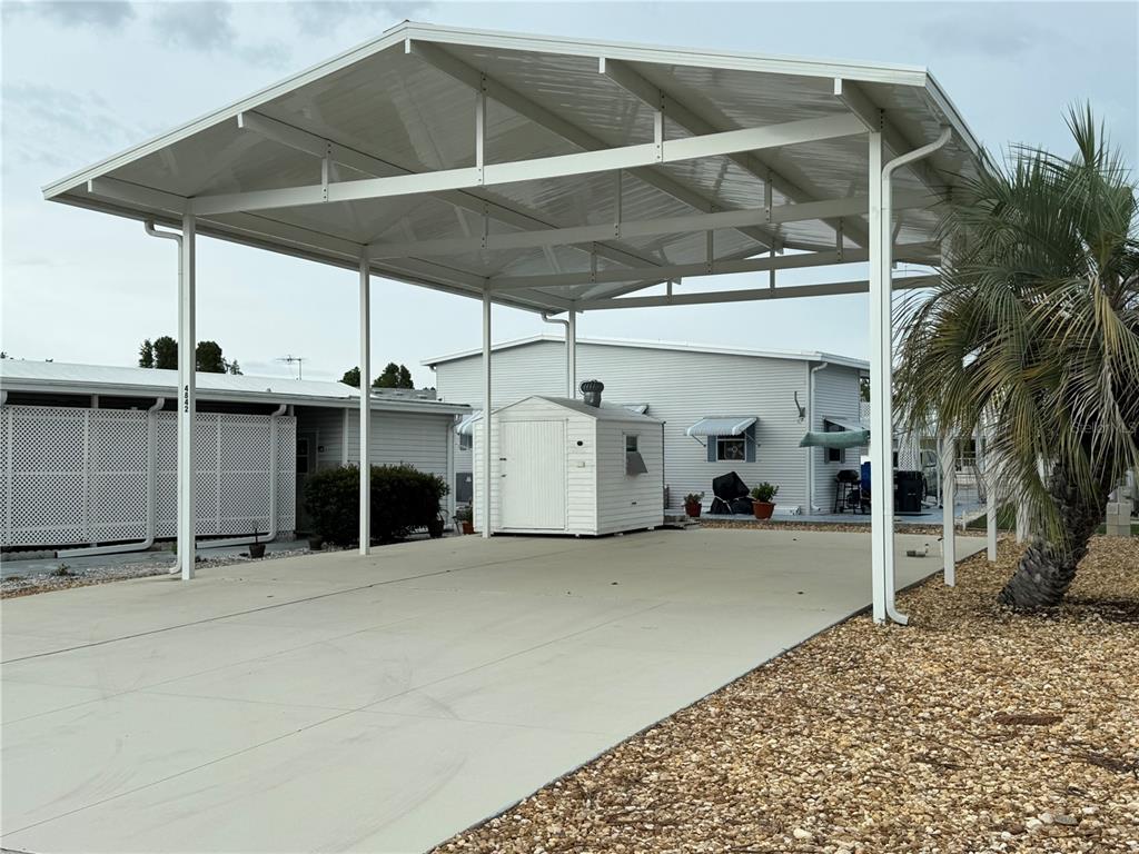 A white metal carport covers a concrete driveway next to a small storage shed — 4842 BOBBY AVENUE Lot 198, ZEPHYRHILLS, FL