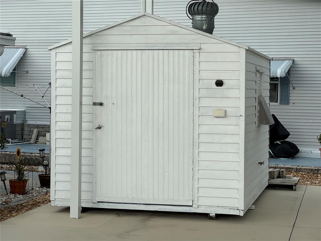 A white, rectangular storage shed with a single door sits on a concrete patio — 4842 BOBBY AVENUE Lot 198, ZEPHYRHILLS, FL