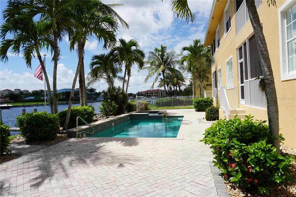 A swimming pool and patio area sit beside a yellow building overlooking a canal — 3216 PURPLE MARTIN DRIVE UNIT 121, PUNTA GORDA, FL