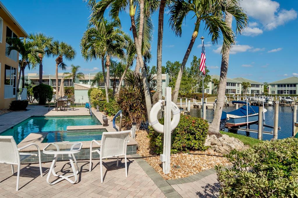 A swimming pool and patio area overlook a boat dock with palm trees and buildings — 3216 PURPLE MARTIN DRIVE UNIT 121, PUNTA GORDA, FL