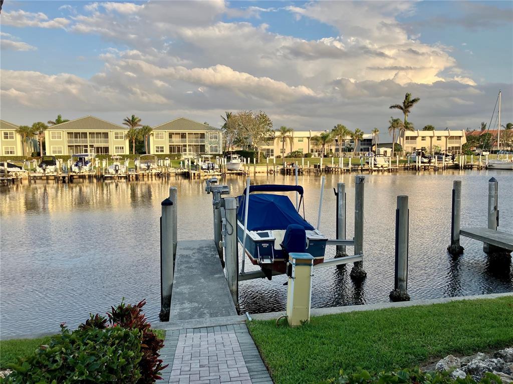 A boat sits on a lift at a dock overlooking a canal and apartment buildings — 3216 PURPLE MARTIN DRIVE UNIT 121, PUNTA GORDA, FL