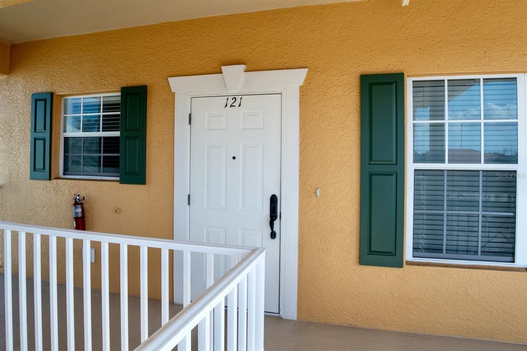 The exterior of a residential unit features a white door numbered 121, green shutters, and a white railing — 3216 PURPLE MARTIN DRIVE UNIT 121, PUNTA GORDA, FL