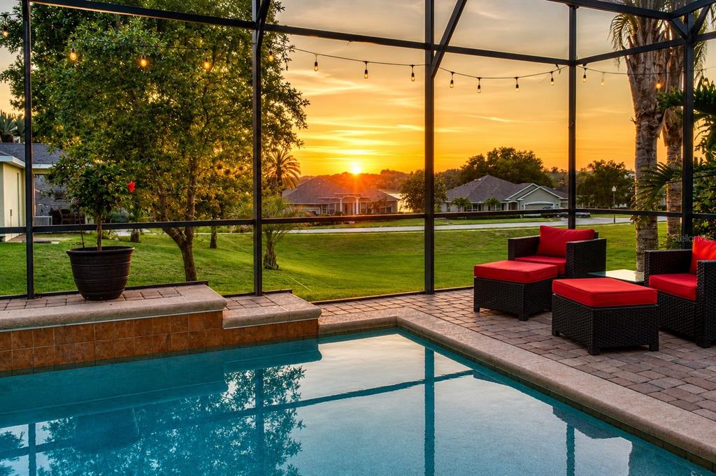 A screened-in patio features a swimming pool, red cushioned chairs, and a sunset lake view — 9223 IVYWOOD STREET, CLERMONT, FL