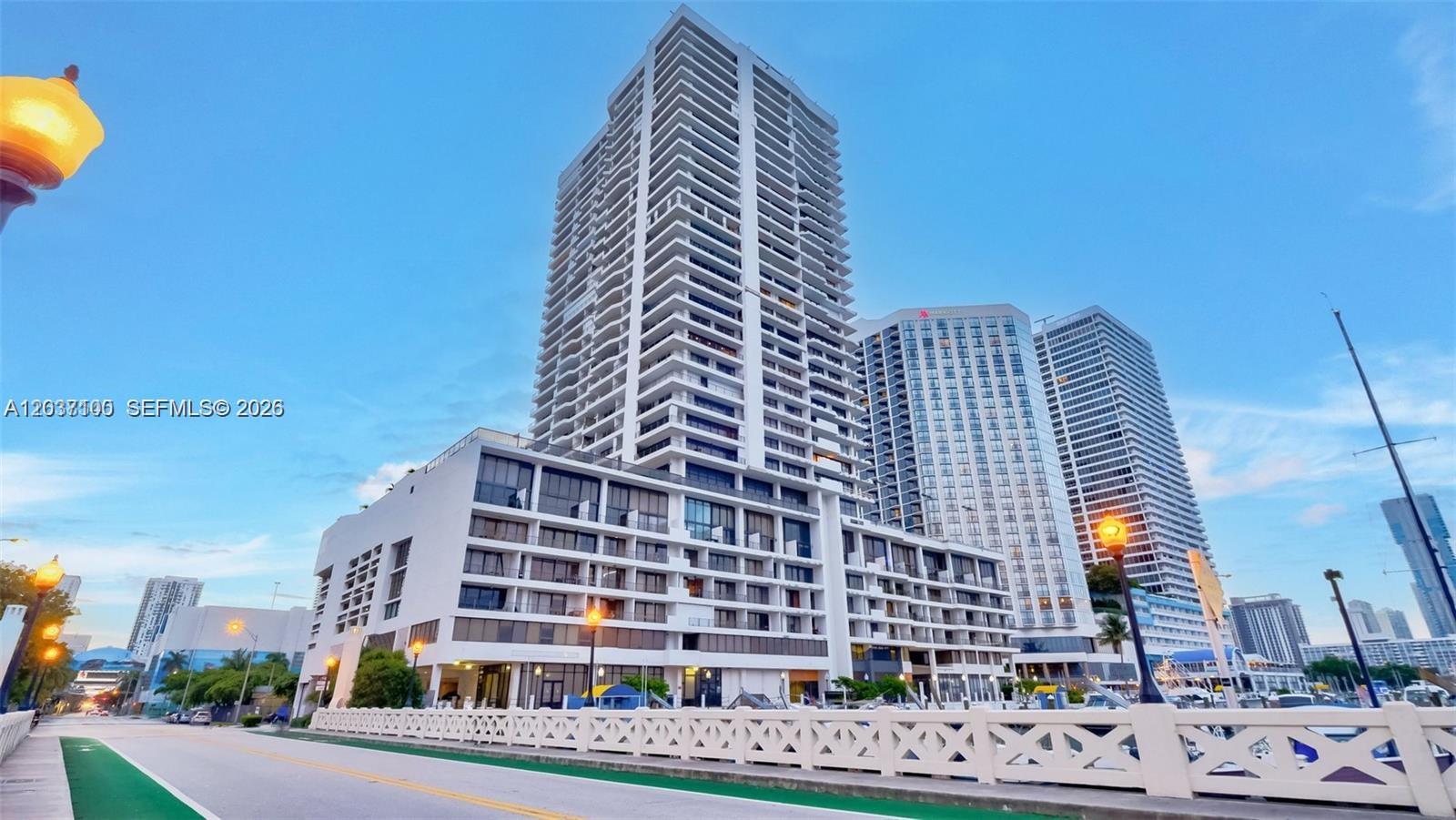 A tall residential building stands beside a road with a white fence in the foreground — 555 NE 15th St # 17E, Miami FL 33132, MIAMI, FL