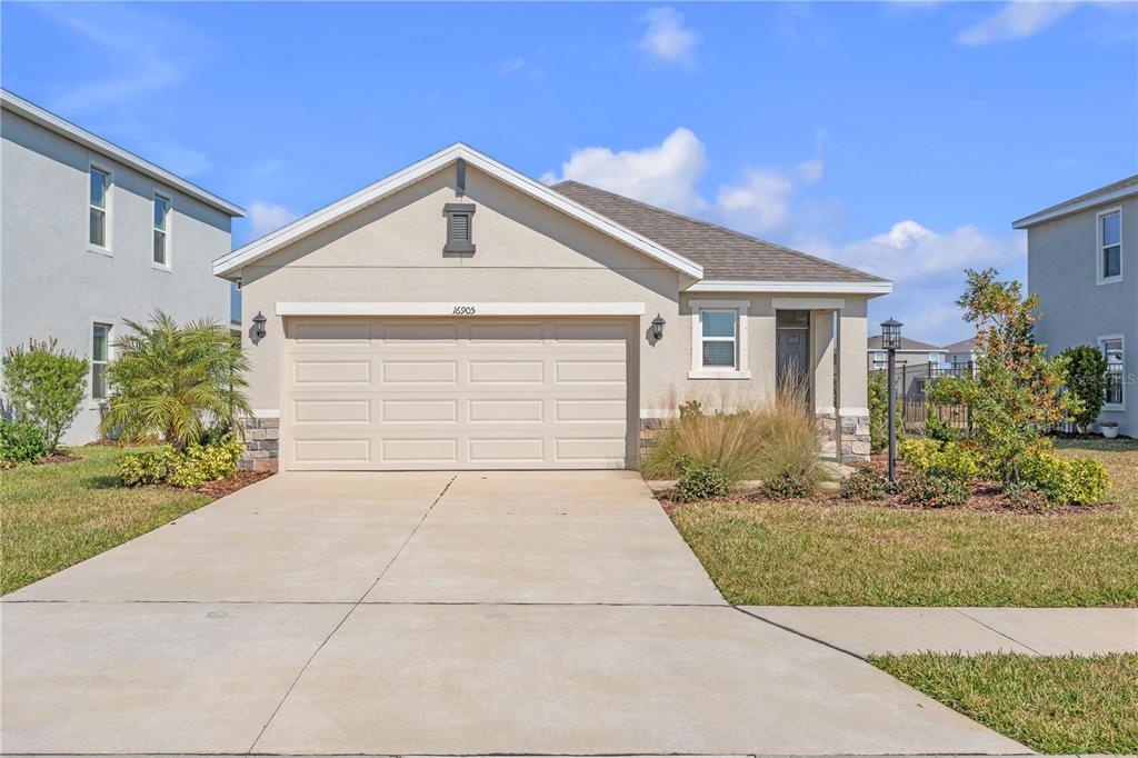 A single-story house with a beige stucco exterior, a two-car garage, and a concrete driveway — 16905 YARD SPRING DRIVE, BRADENTON, FL