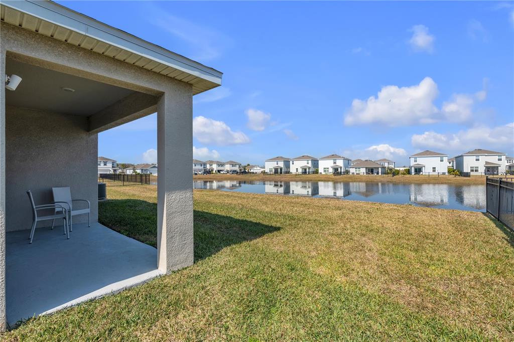 A covered patio overlooks a grassy backyard and a pond with houses in the distance — 16905 YARD SPRING DRIVE, BRADENTON, FL