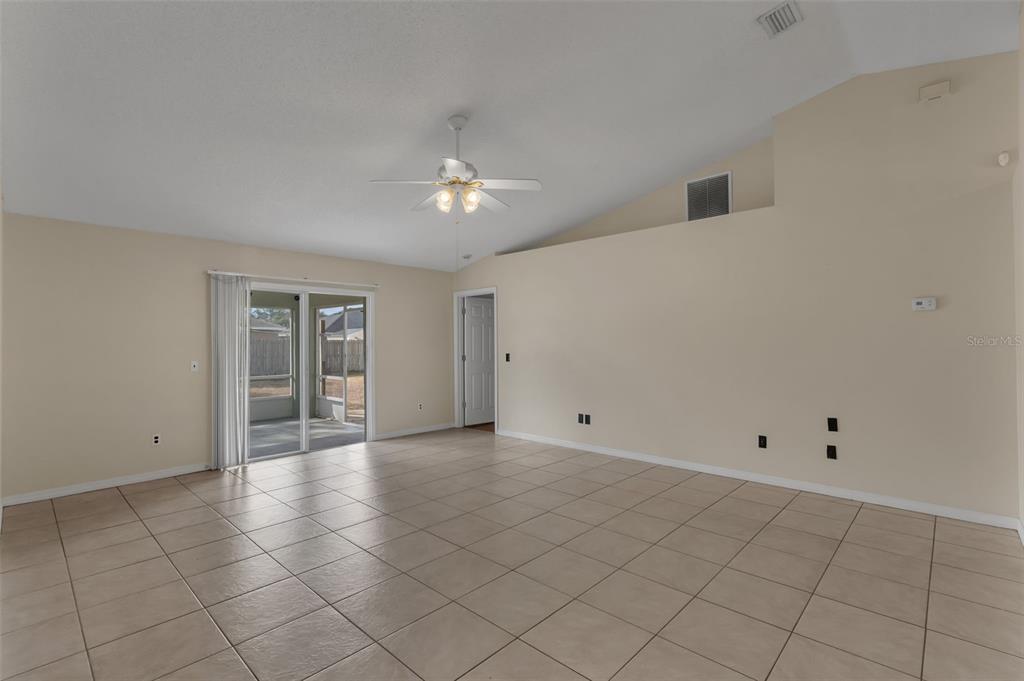 An empty living room features beige tile flooring, a vaulted ceiling with a fan, and sliding doors — 36 PINE HILL LANE, PALM COAST, FL