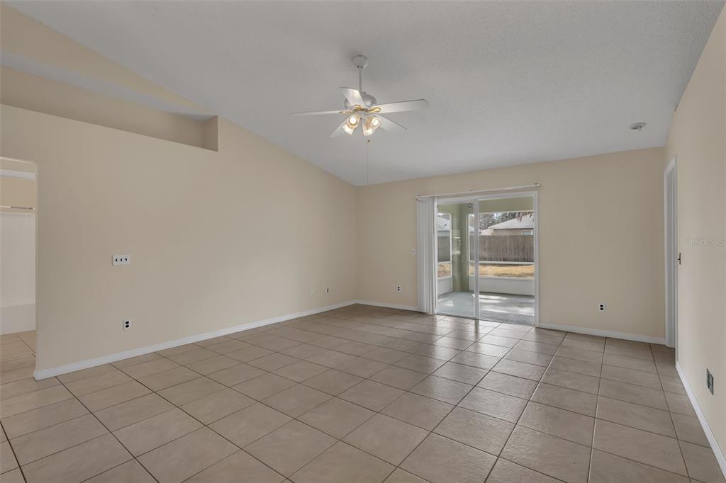 An empty living room features beige tile flooring, a vaulted ceiling, and sliding glass doors — 36 PINE HILL LANE, PALM COAST, FL