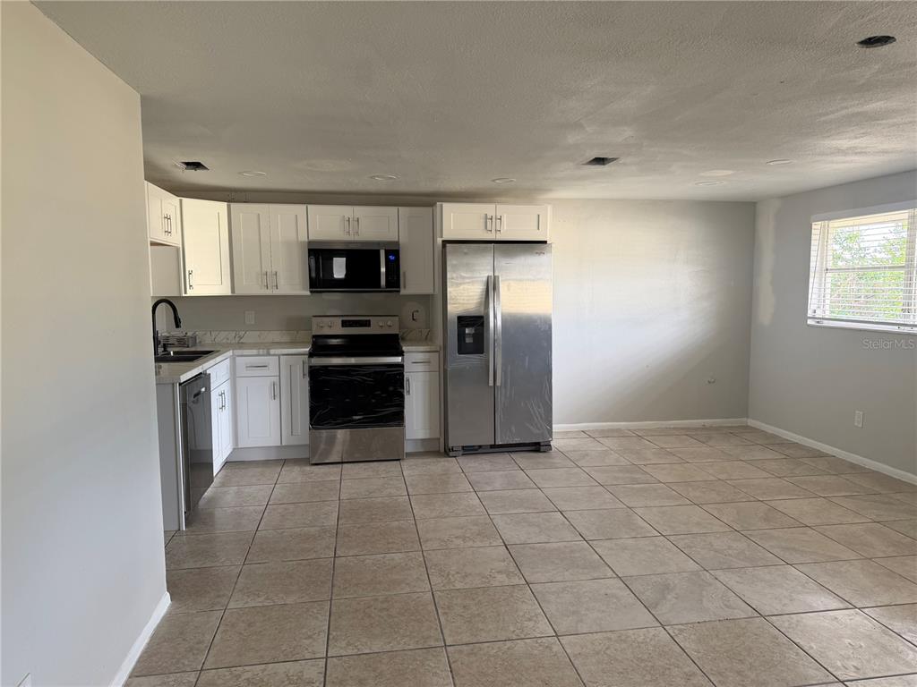 A kitchen features white cabinets, stainless steel appliances, and light-colored tile flooring — 3009 W WATERS AVENUE, TAMPA, FL