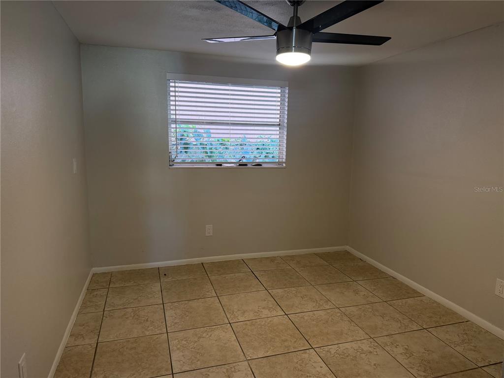 An empty room features light-colored walls, tiled flooring, a ceiling fan, and a single window — 3009 W WATERS AVENUE, TAMPA, FL