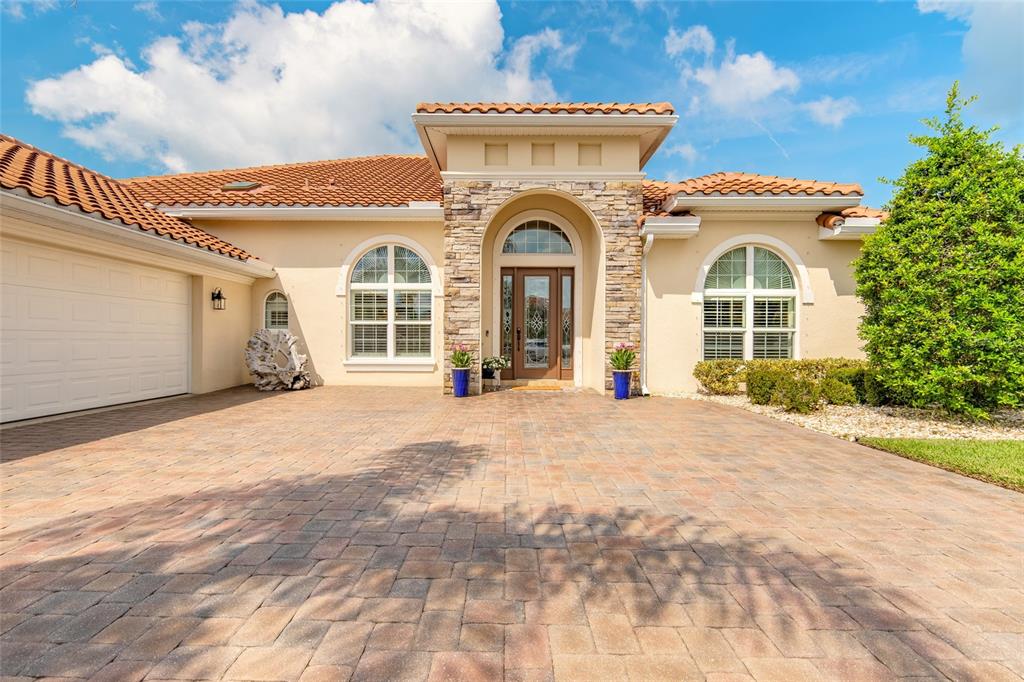 The exterior of a single-story house features a stone-accented entryway, arched windows, and a paver driveway — 2909 N ASCIANO COURT, NEW SMYRNA BEACH, FL