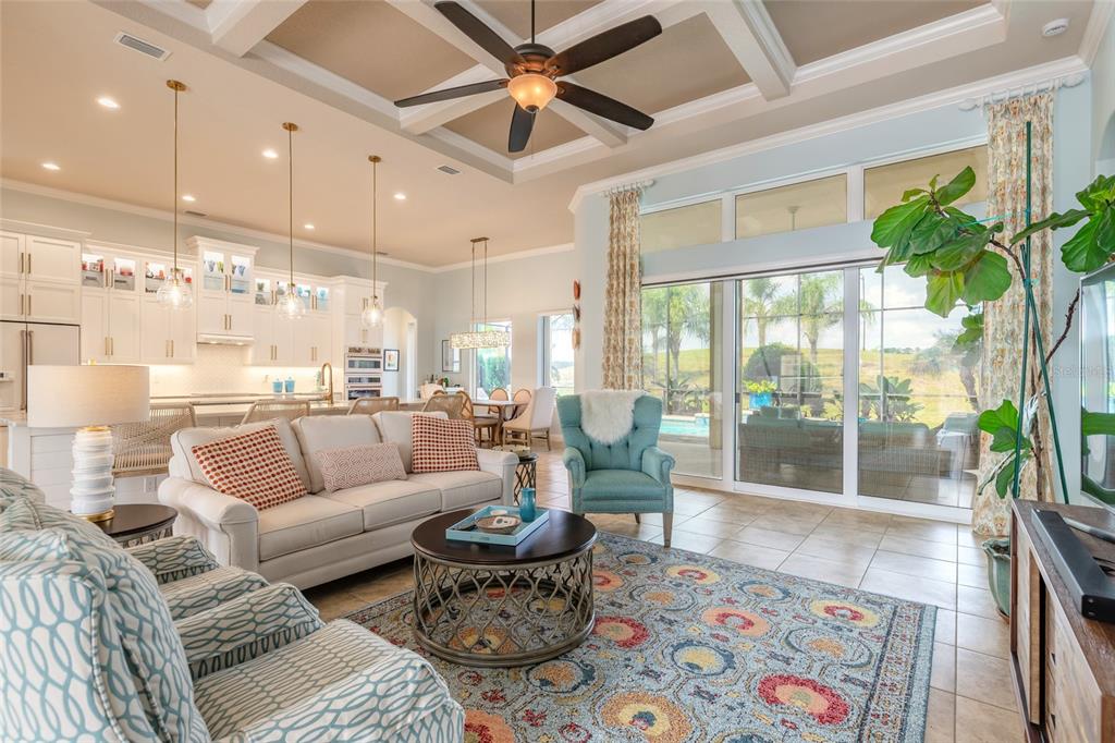 A bright open-concept living room with a coffered ceiling, tile floors, and sliding glass doors — 2909 N ASCIANO COURT, NEW SMYRNA BEACH, FL