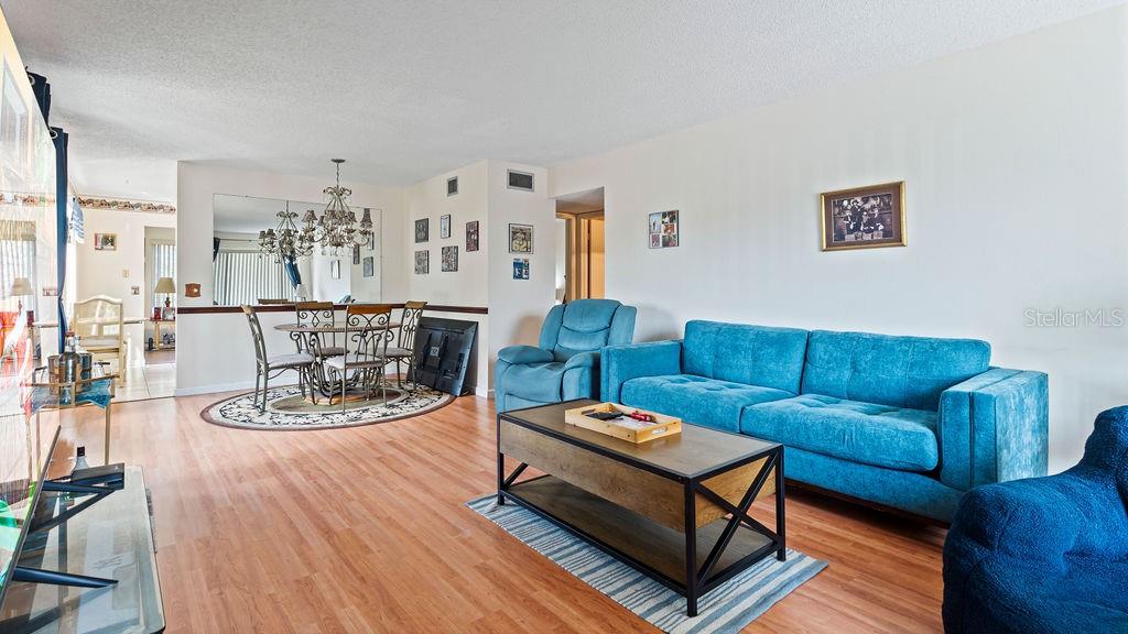 A living room with wood-look flooring features a blue sofa, a coffee table, and a dining area — 2370 JAMAICAN STREET UNIT 30, CLEARWATER, FL
