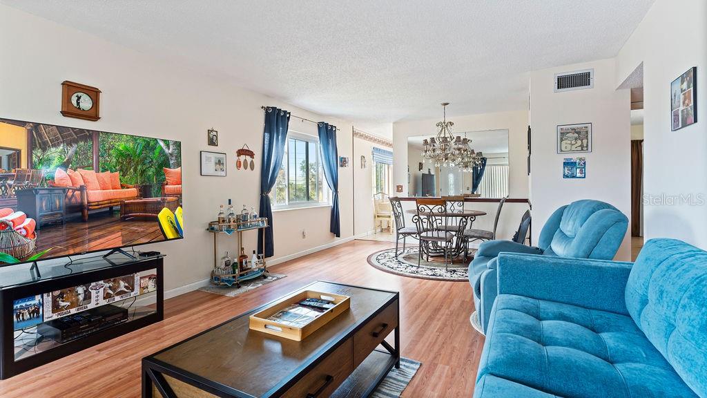 A living room and dining area with wood-look flooring, blue furniture, and a large television — 2370 JAMAICAN STREET UNIT 30, CLEARWATER, FL