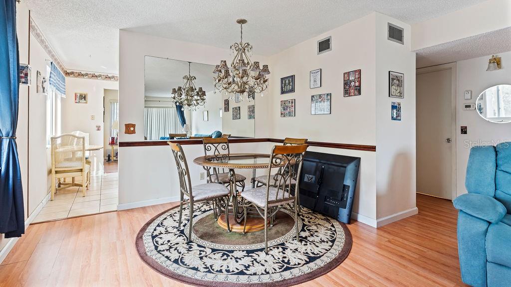 A dining area features a glass-top table, metal chairs, a chandelier, and a round rug — 2370 JAMAICAN STREET UNIT 30, CLEARWATER, FL