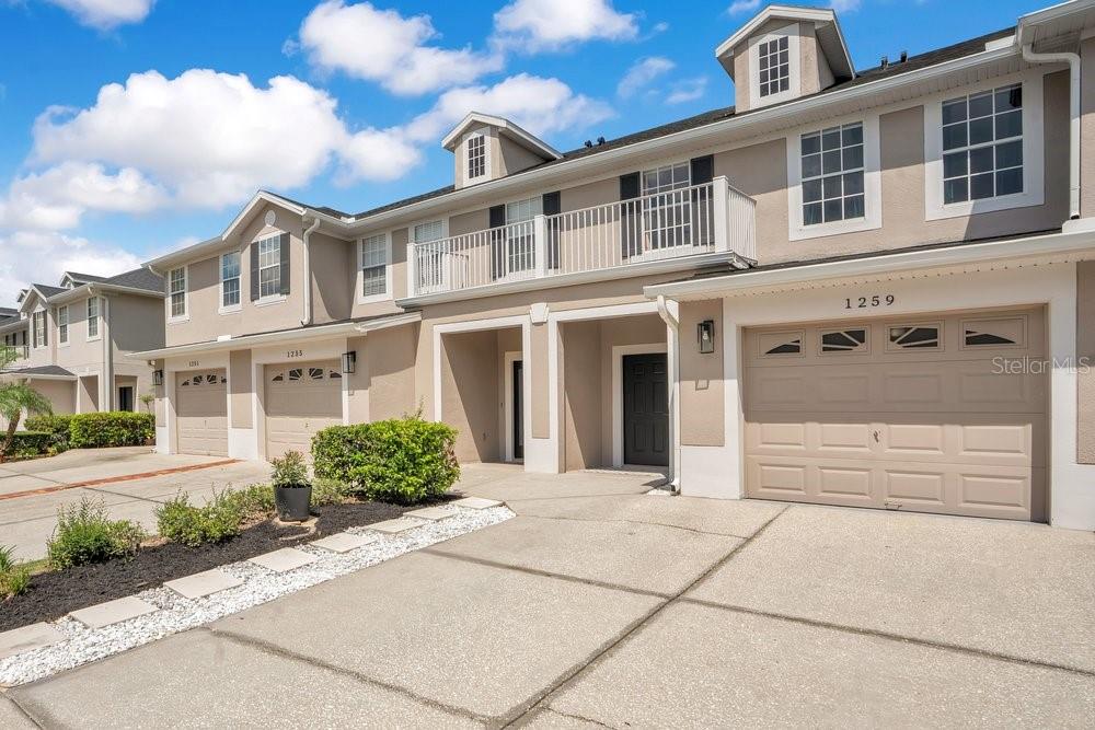 A row of two-story townhomes with beige stucco siding, attached garages, and upper-level balconies — 1259 FALLING STAR LANE, ORLANDO, FL