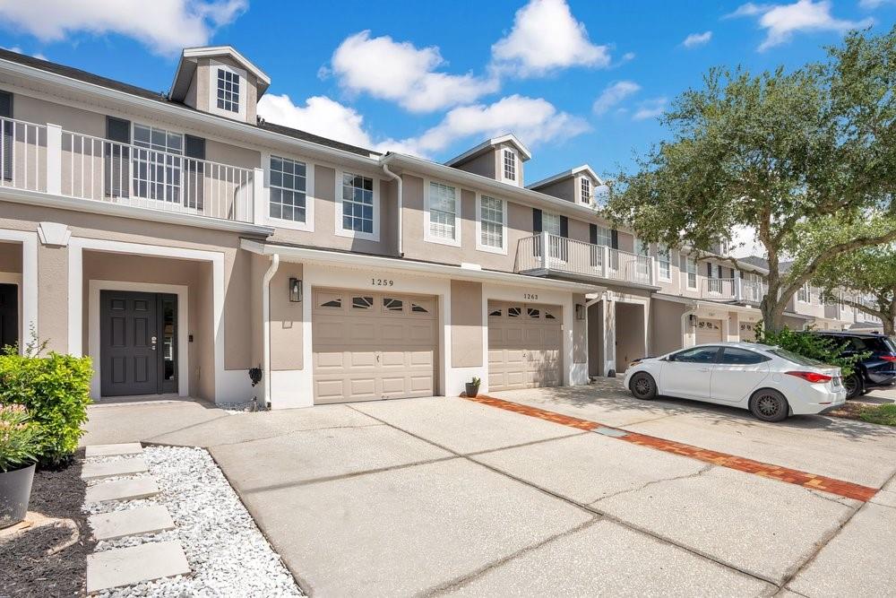 A row of multi-story townhomes with beige stucco facades, attached garages, and concrete driveways — 1259 FALLING STAR LANE, ORLANDO, FL