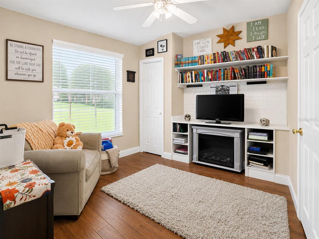 A living room features a fireplace, built-in shelving, a television, and a beige armchair — 2408 SE 23RD PLACE, OCALA, FL