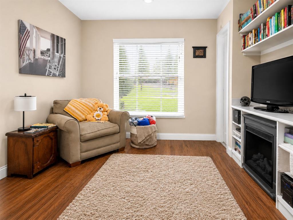 A cozy living room features a beige armchair, a fireplace with a television, and bookshelves — 2408 SE 23RD PLACE, OCALA, FL