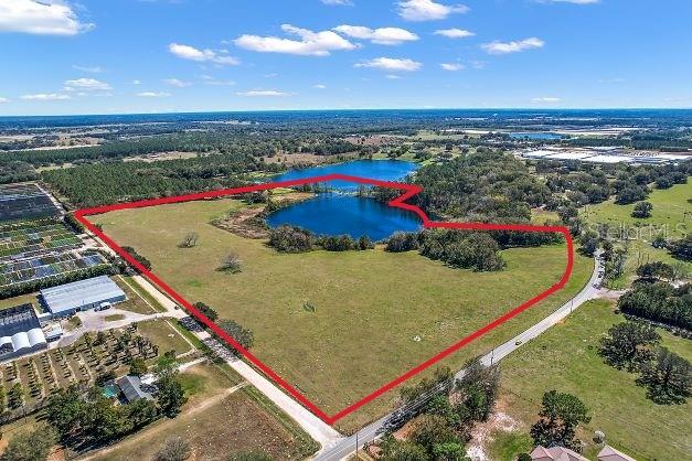 An aerial view shows a large, open grassy field outlined in red with a central pond — BRITT ROAD AND FUTURE FARM DRIVE, MOUNT DORA, FL