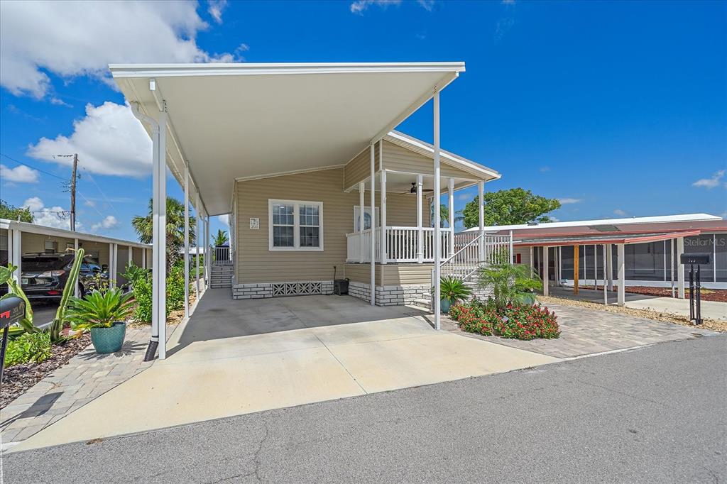 A tan mobile home features a large attached carport and a small front porch — 203 BIMINI DRIVE, PALMETTO, FL