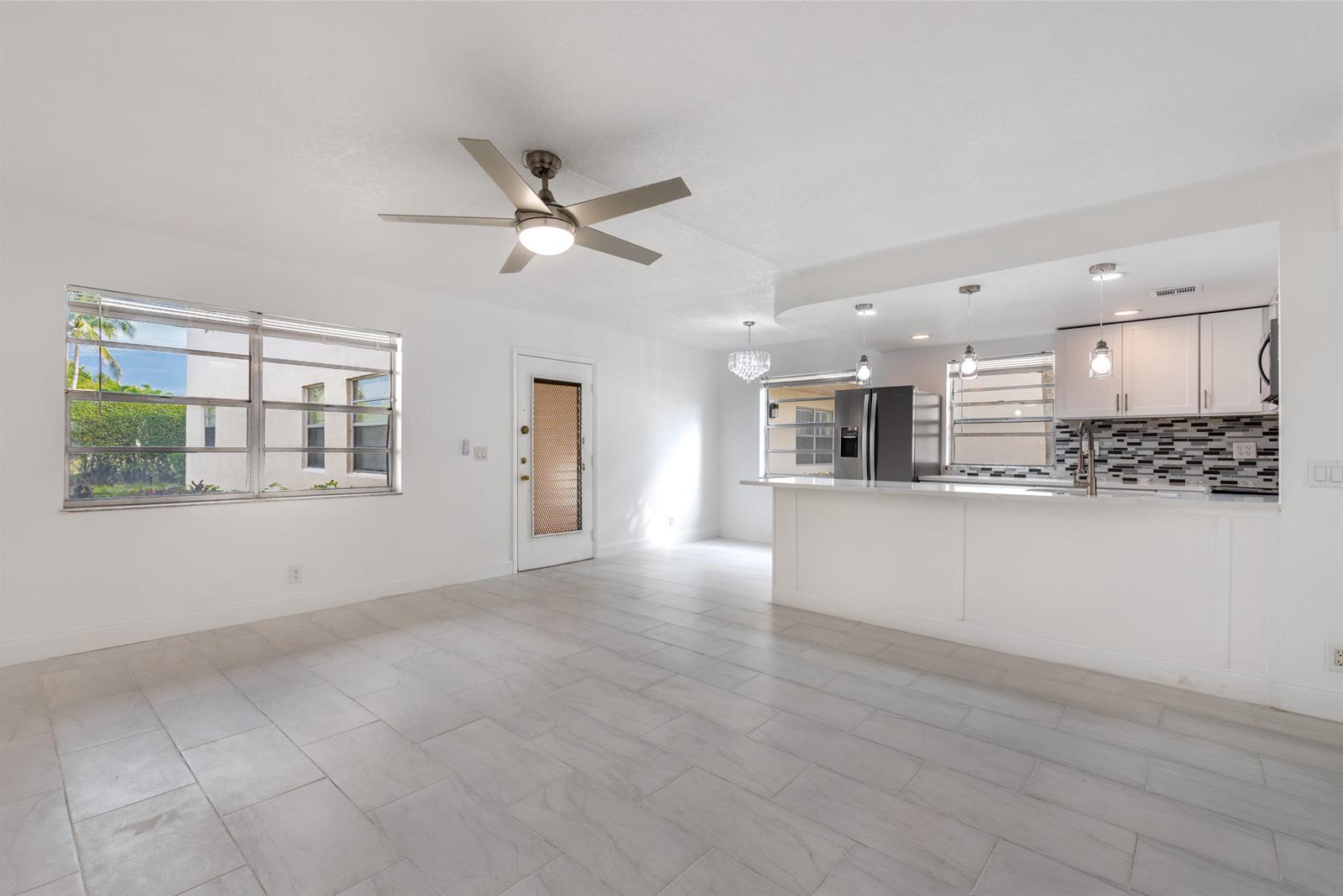 A bright, open-concept living and kitchen area features white walls, tile flooring, and a ceiling fan — 108 Normandy Lane # C, Delray Beach FL 33484, DELRAY BEACH, FL