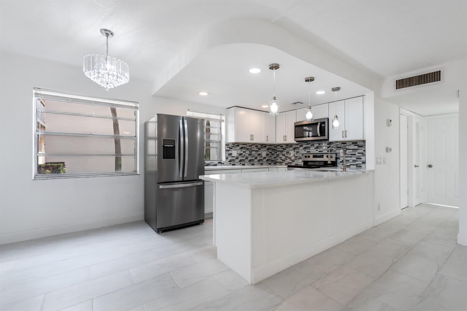 A modern kitchen features white cabinets, stainless steel appliances, a breakfast bar, and tile flooring — 108 Normandy Lane # C, Delray Beach FL 33484, DELRAY BEACH, FL