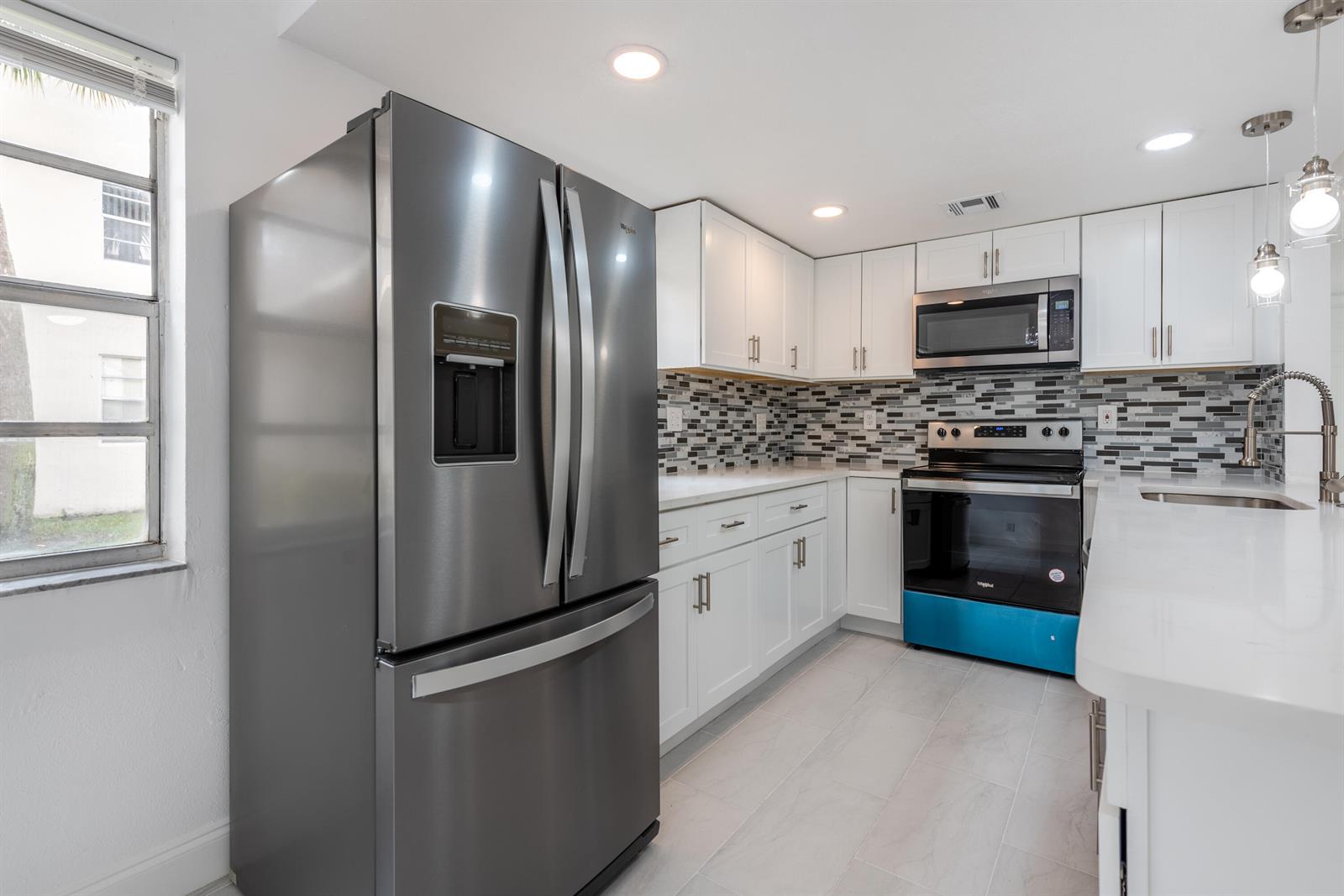A kitchen features white cabinets, stainless steel appliances, a mosaic backsplash, and light-colored tile flooring — 108 Normandy Lane # C, Delray Beach FL 33484, DELRAY BEACH, FL