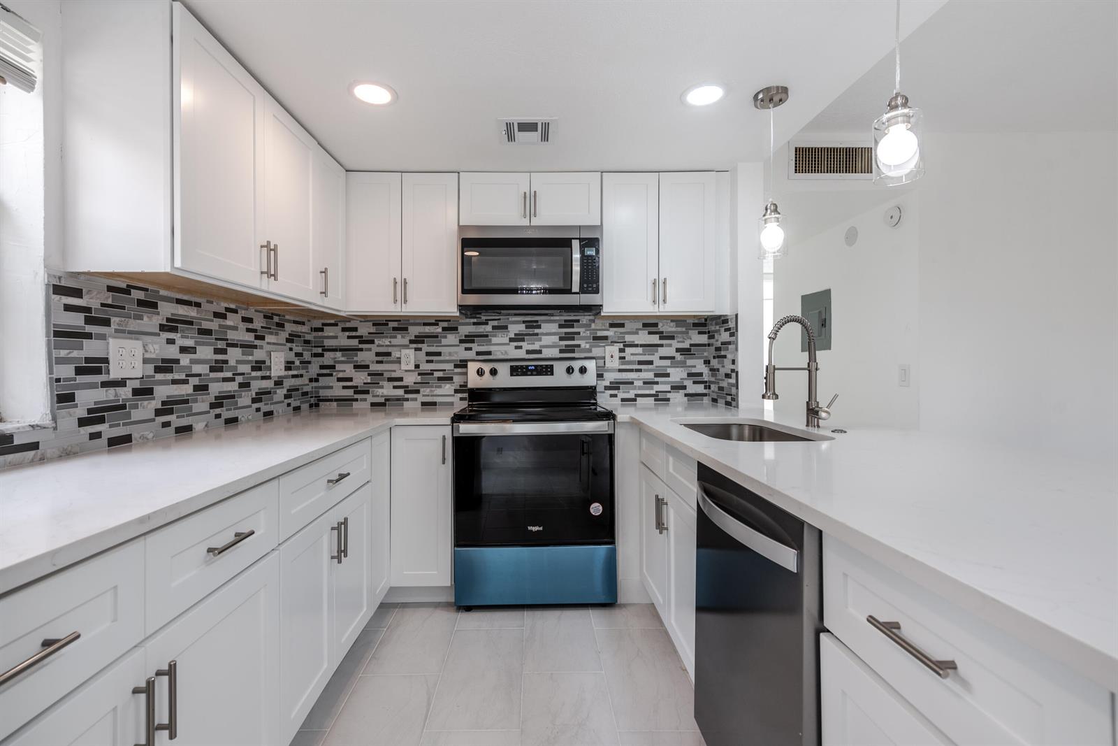 A kitchen with white cabinets, quartz countertops, a mosaic tile backsplash, and stainless steel appliances — 108 Normandy Lane # C, Delray Beach FL 33484, DELRAY BEACH, FL