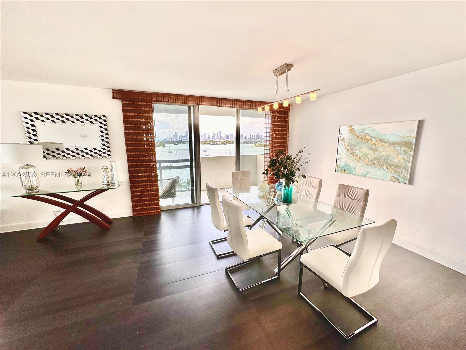 A dining room features a glass table, white chairs, dark flooring, and a waterfront balcony view — 1500 Bay Rd # 1114S, Miami Beach FL 33139, MIAMI BEACH, FL