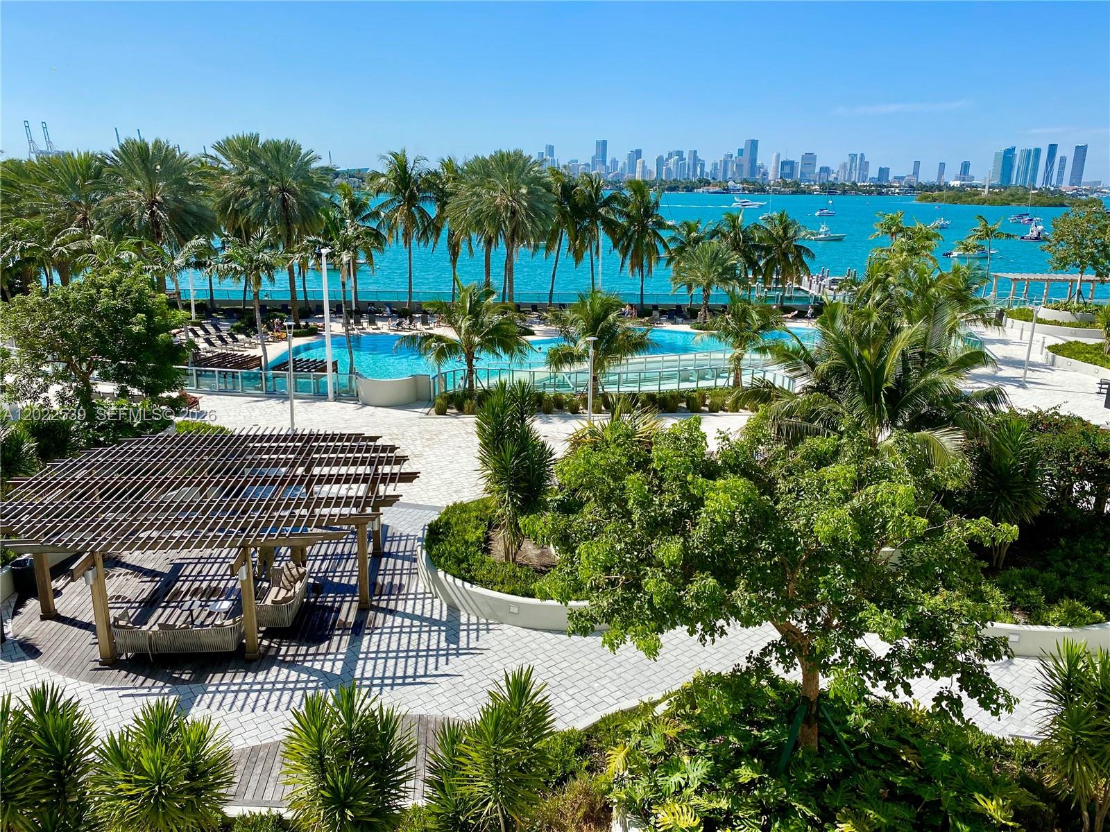 An outdoor pool area features palm trees, a wooden pergola, and a view of the skyline — 1500 Bay Rd # 1114S, Miami Beach FL 33139, MIAMI BEACH, FL