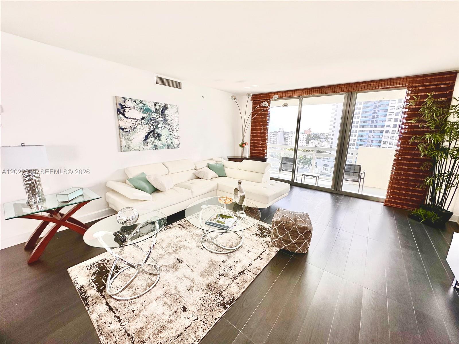 A living room features a white sectional sofa, glass tables, and dark wood flooring — 1500 Bay Rd # 1114S, Miami Beach FL 33139, MIAMI BEACH, FL